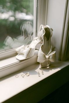 a pair of white shoes sitting on top of a window sill next to a pair of earrings