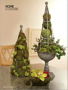 a table topped with two metal vases filled with plants