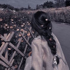 a woman sitting on top of a wooden bench next to a lush green field covered in flowers