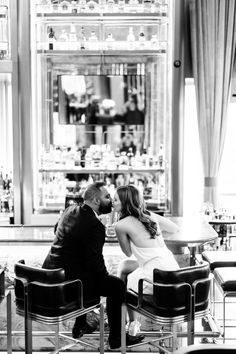 a man and woman sitting at a table in front of a bar kissing each other