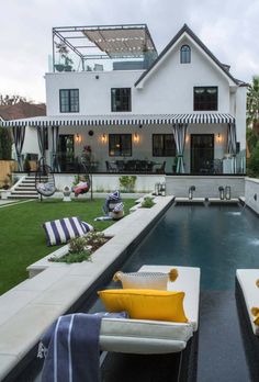 an outdoor swimming pool with lounge chairs and pillows on the grass next to it in front of a large white house