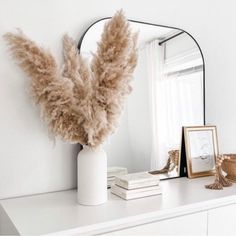 a white dresser topped with a mirror and a vase filled with feathers