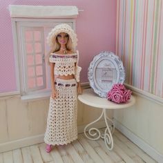 a doll is standing next to a table with a plate and pink roses on it