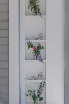 a shelf filled with flowers and shoes on top of a white wall next to a door