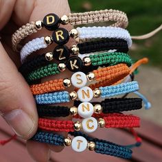 a person holding several bracelets with letters and beads on them, all in different colors