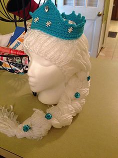 a white mannequin head with a blue crown on it's head sitting on a counter