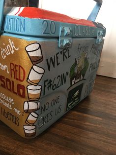 a suitcase that has been painted with different colors and designs on the side, sitting on a wooden floor