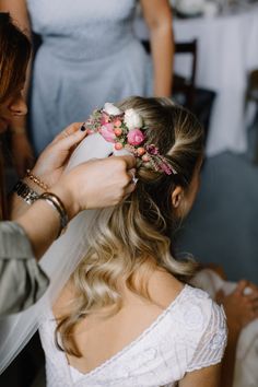 the bride is getting ready to put her flower crown on her head while another woman looks on