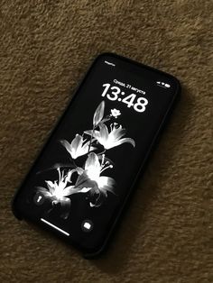 an iphone with flowers on the screen sitting on carpeted floor next to phone charger