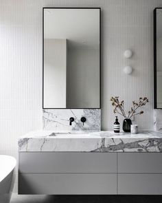 a bathroom with marble counter tops and two mirrors on the wall, along with a white bathtub