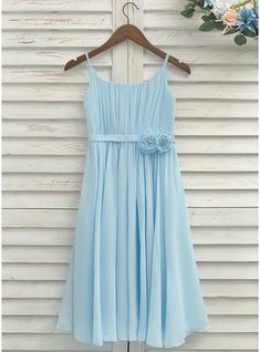 a light blue dress hanging on a wooden hanger with flowers in front of it