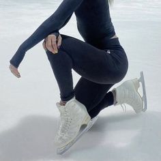 a woman in black shirt and leggings skating on ice rink with her hands behind her back