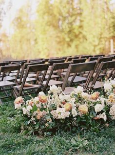 rows of wooden chairs with flowers on them in an outdoor ceremony area at a wedding