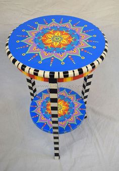 an artistically painted table with striped legs and a flower design on the top, sitting on a white background