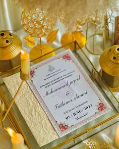 a table topped with lots of candles next to a white and gold wedding card on top of a table