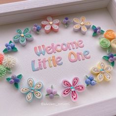 a welcome little one frame with flowers and butterflies on it's side in a white shadow box