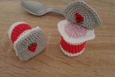 two crocheted cupcakes sitting on top of a wooden table next to a spoon