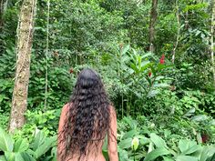 a woman with long hair walking through the jungle