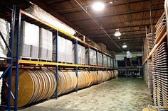 there are many stacks of wooden barrels in the warehouse with lights above them and behind them is a rack full of wood planks