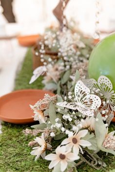 an arrangement of flowers and plates on a mossy table cloth with green apples in the background