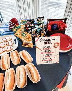 a table topped with hot dogs covered in toppings and other snacks on plates next to a sign