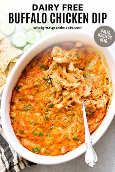 a bowl filled with chicken dip next to chips and cucumber slices on the side