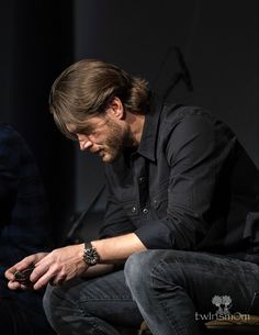 a man sitting on top of a chair next to another man holding a cell phone