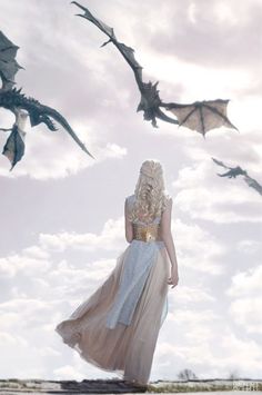 a woman standing in front of two flying dragon like birds on a cloudy day with her back to the camera