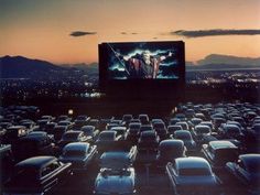 an outdoor movie screen in the middle of a parking lot filled with cars at night