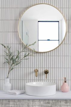 a white sink sitting under a round mirror next to a vase with a plant in it