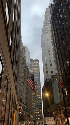 an american flag is flying in the sky between two tall buildings on a city street