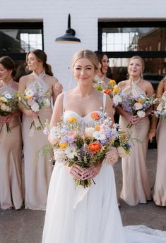 the bride and her bridal party are all dressed in neutral colored gowns, holding their bouquets