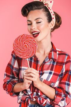 a woman holding a lollipop in her hands and smiling at the camera on a pink background