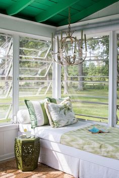 a bed sitting under a window next to a green lamp and a chandelier