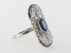 Vintage Filigree Cocktail Ring Art Deco Sapphire in Platinum $5,250.00 Vintage Filigree Cocktail Ring Art Deco Sapphire in Platinum. The center oval sapphire is approximately 1.20 carats and is a slightly darker royal blue with medium transparency. The platinum open filigree is set with rose cut diamonds. The border of this unique Art Deco oval shaped cocktail ring is set with french cut sapphires creating a frame around this lovely ring. Composition: Platinum Ring Size: 6.75 Center Stone Shape: Oval Platinum Sapphire Ring, Oval Diamond Cut Sapphire Ring Fine Jewelry, Oval Sapphire Ring With Diamond Cut In Platinum, Oval Sapphire Diamond Ring With Diamond Cut, Art Deco Oval Sapphire Ring In Platinum, Oval Sapphire Ring In Platinum, Blue Oval Sapphire Ring In Art Deco Style, Art Deco Blue Oval Sapphire Ring, Antique Oval Sapphire Ring In Platinum