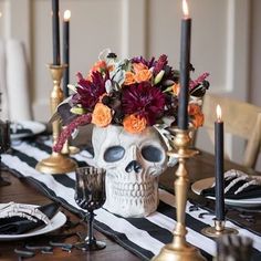 a table topped with a skull vase filled with flowers and candles on top of it