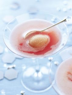 two martini glasses filled with pink liquid and a gold heart on the rim, sitting on a blue tablecloth