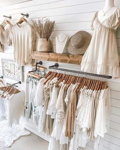 clothes and hats are hanging on racks in a clothing store, with white walls behind them