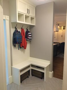 a white bench with two coats hanging on the wall and some drawers in front of it