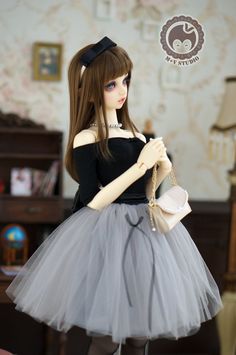 a doll is dressed in a black top and grey tutu skirt, holding a purse