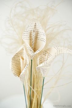 an arrangement of flowers made out of book pages in a vase filled with dry grass