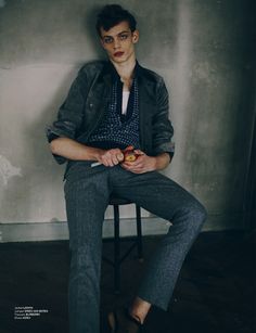 a young man sitting on top of a chair holding an apple in his hand and looking at the camera