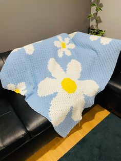 a blue and white crocheted blanket sitting on top of a black leather couch