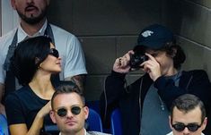 two men and a woman sitting next to each other in the stands at a baseball game