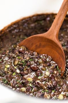 a wooden spoon in a pot filled with black beans and other food items on a white surface