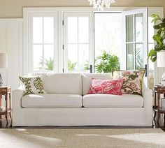 a living room filled with furniture and a chandelier hanging from the ceiling next to two windows