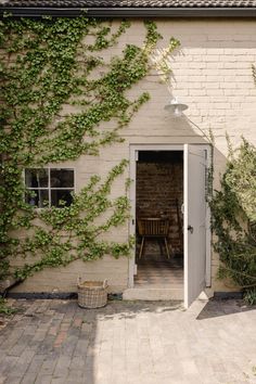 an open door to a small house with vines growing on the outside wall and brick patio