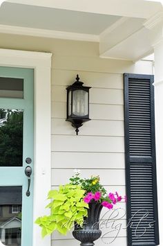 a lamp on the side of a house with flowers in front of it and a blue door