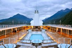 the deck of a cruise ship with a swimming pool and mountain range in the background