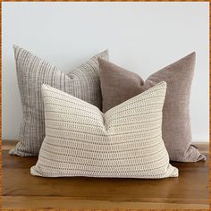 three pillows sitting on top of a wooden table next to each other, one in grey and the other in white